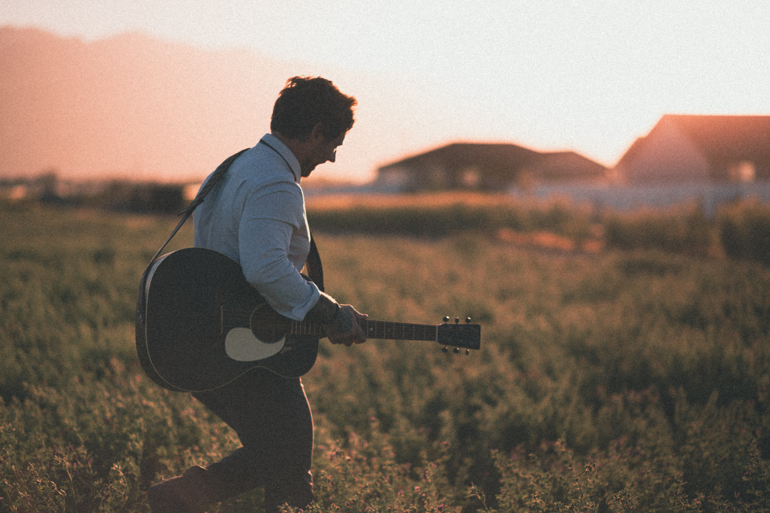 Casey Ryan walking through a field with his guitar at golden hour