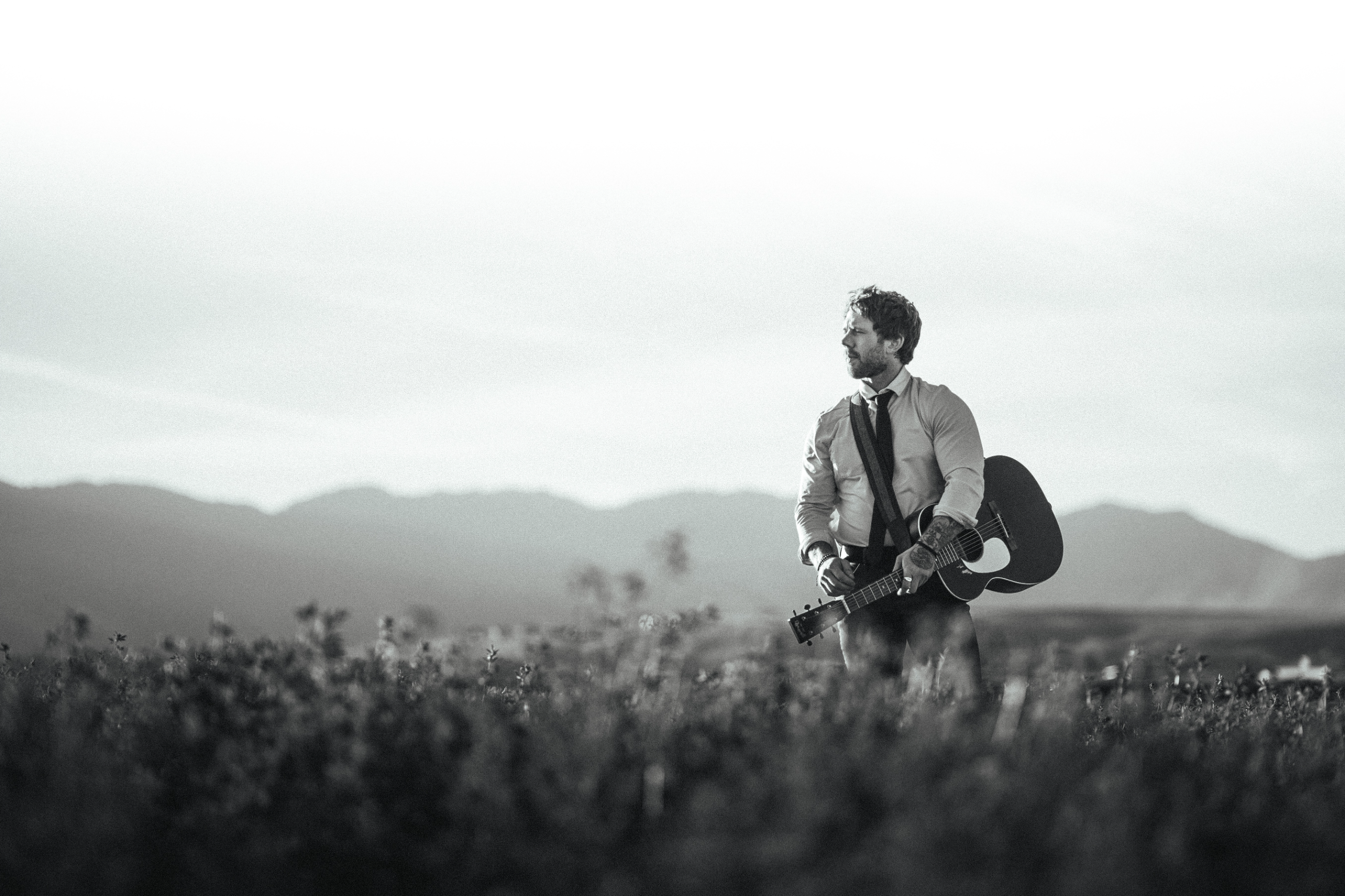 Casey Ryan with his acoustic guitar in an open field
